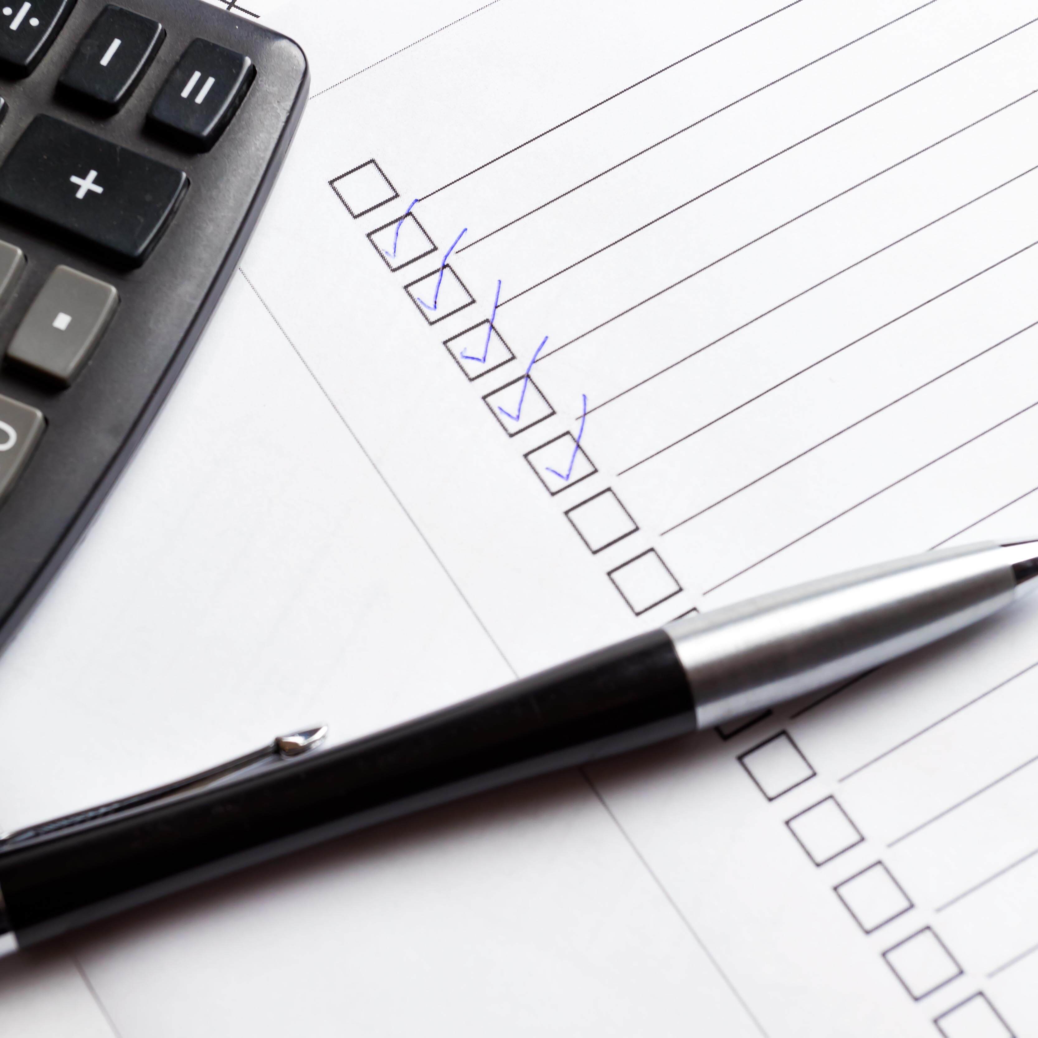 Ticked boxes on check list with elegant pen and calculator.