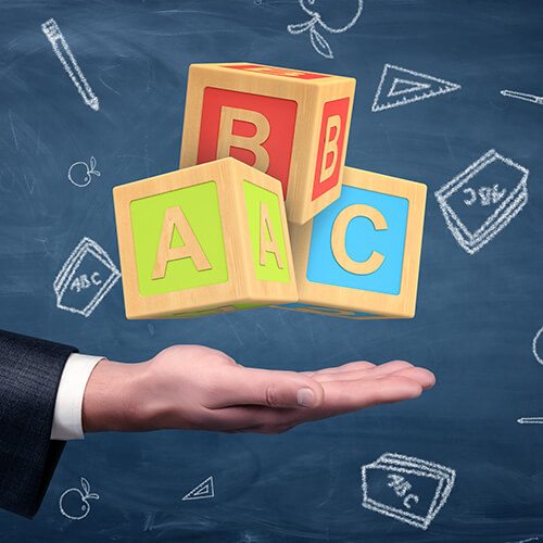 Man's hand holding ABC blocks against chalkboard